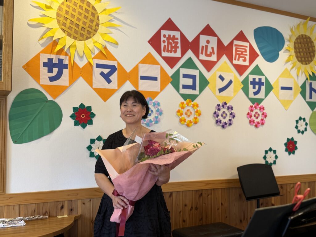 ホームコンサートの飾り付けの前で花束を手にする小池さん